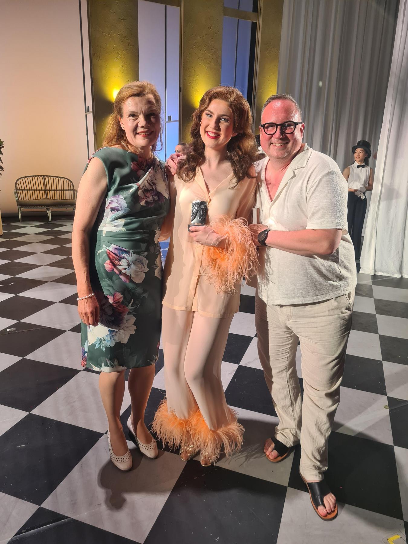 Bettina Post, Małgorzata Rocławska und Hendrik Müller stehen auf der Bühne und lächeln fröhlich in die Kamera.
