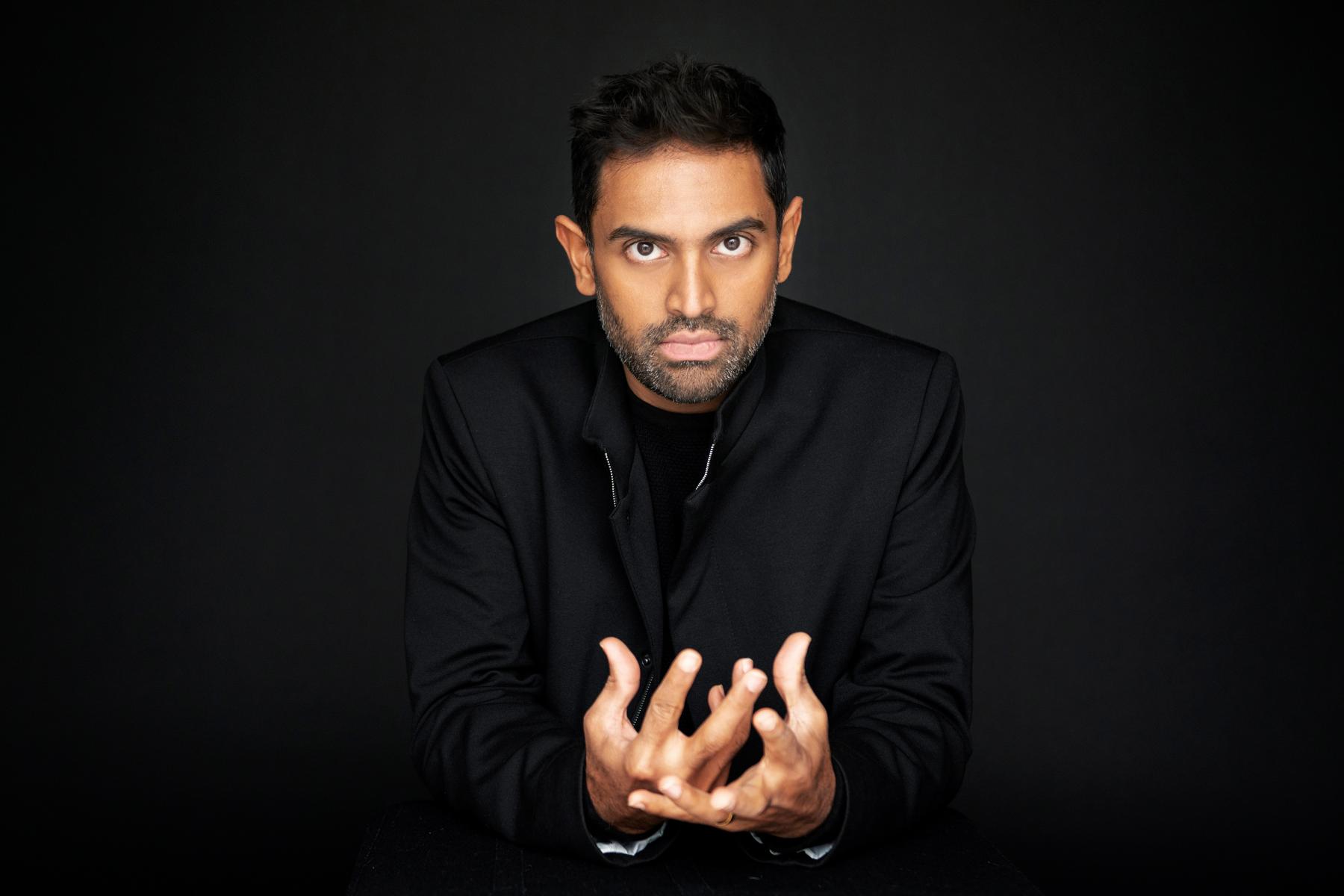 Portrait eines Mannes vor dunklem Hintergrund, er führt die Hände dramatisch vor seinem Körper zusammen.