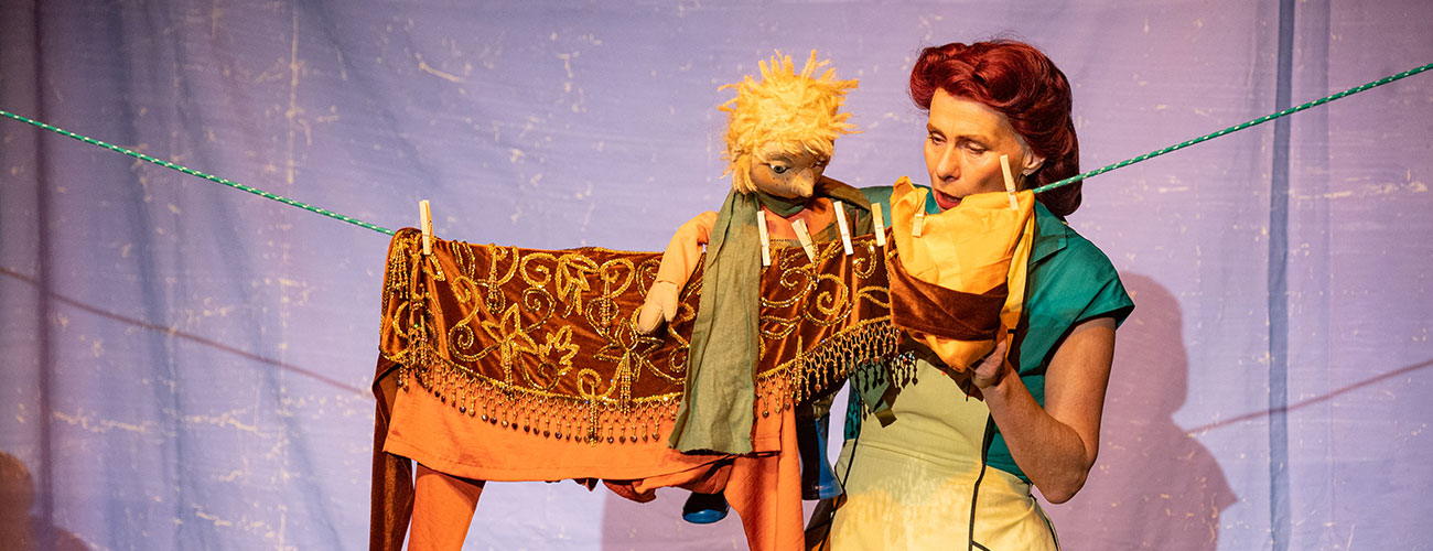Szene aus dem Puppenspiel HANS IM GLÜCK, Sonja Langmack mit einer Handpuppe hinter einer Wäscheleine