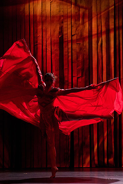 Auf einer dunklen Bühne tanzt eine junge Frau in einem wehenden roten Kostüm