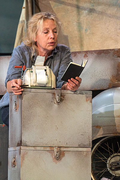 Szenenfoto aus MUTTER COURAGE UND IHRE KINDER, eine blonde Frau steht über zwei Kisten gebeugt, sie liest in einem kleinen schwarzen Buch