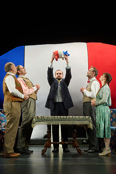 5 Personen stehen vor einem gigantischen Sparschwein in den Farben der französischen Flagge, einer von ihnen hält ein kleines Sparschwein in den gleichen Farben über seinen Kopf, die anderen beobachten es