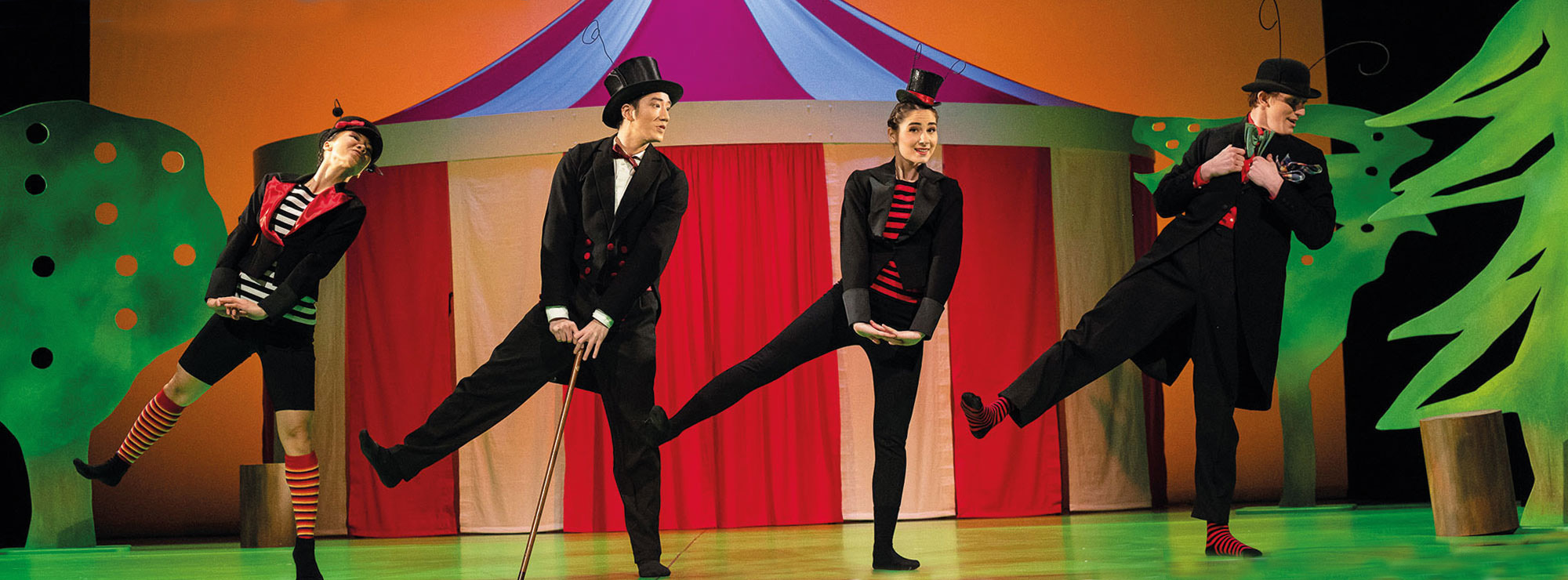 Szene aus DER KARNEVAL DER TIERE, vier Käfer tanzen vergnügt vor einer bunten Zirkuslandschaft