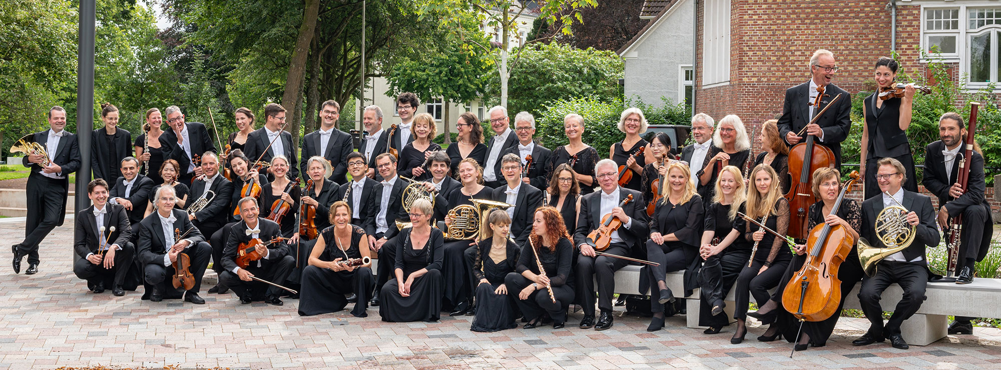 Das Schleswig-Holsteinische Sinfonieorchester, draußen, in schwarzer Kleidung, mit den Instrumenten