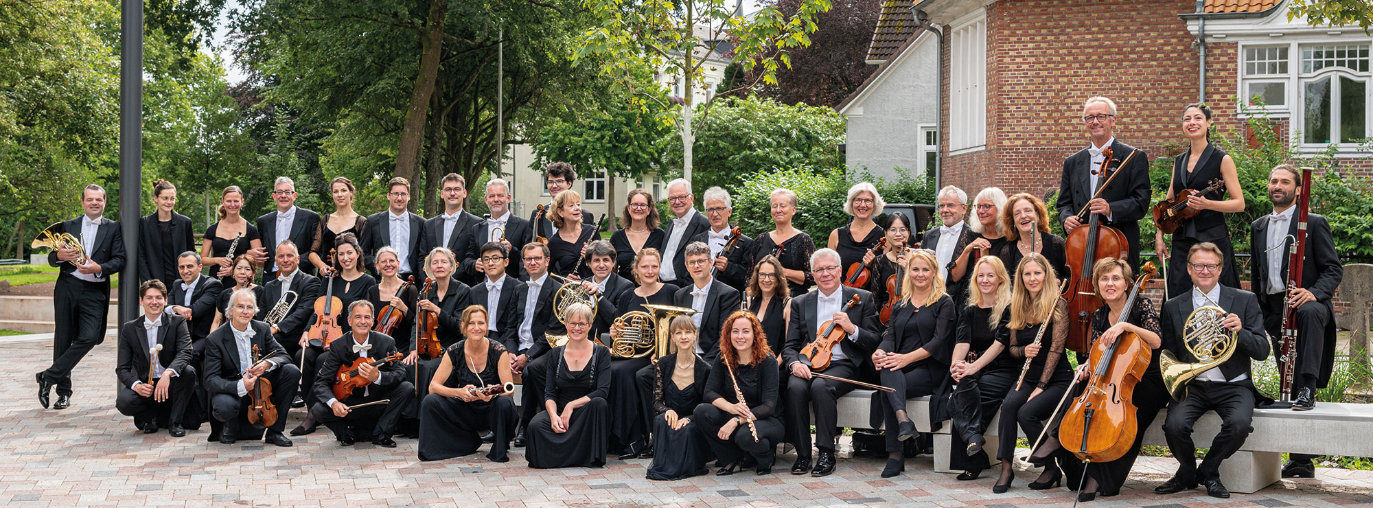 Das Schleswig-Holsteinische Sinfonieorchester, draußen, in schwarzer Kleidung, mit den Instrumenten