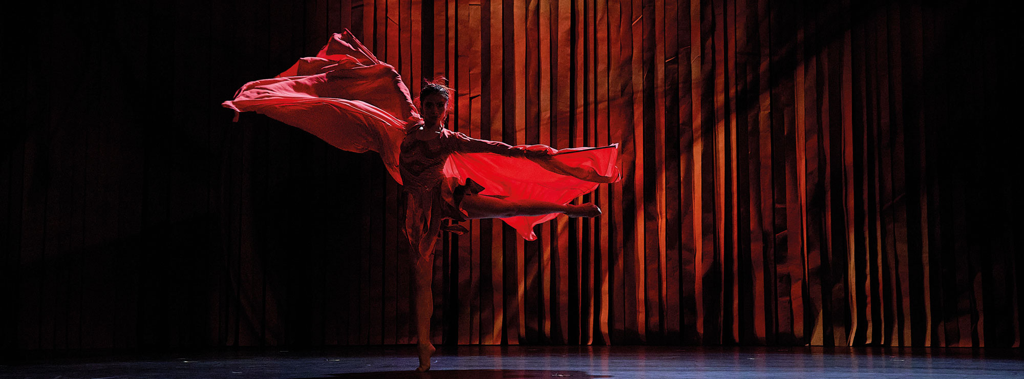 Aus DER FEUERVOGEL, eine Tänzerin auf der dunklen Bühne, sie trägt ein rotes Kleid